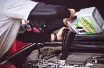 man refilling motor oil on car engine bay